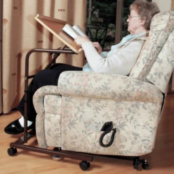 Person reading a book using an over armchair table with adjustable top.