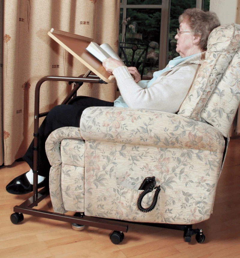 Person reading a book using an over armchair table with adjustable top.