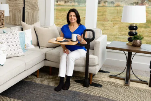 Person using a swivel table attached to a sofa, holding a mug and plate.
