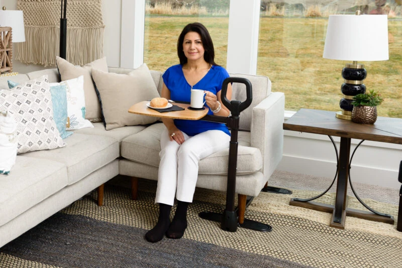 Person using a swivel table attached to a sofa, holding a mug and plate.