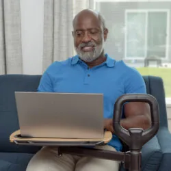 Man sitting on a sofa using a laptop on a rotating tray attached to a handle.