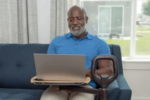 Man sitting on a sofa using a laptop on a rotating tray attached to a handle.