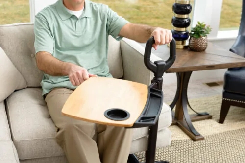 Person using a sitting to standing aid with a wooden tray and handle.
