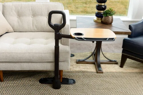 Sitting to standing aid with a dual pivoting tray next to a sofa.