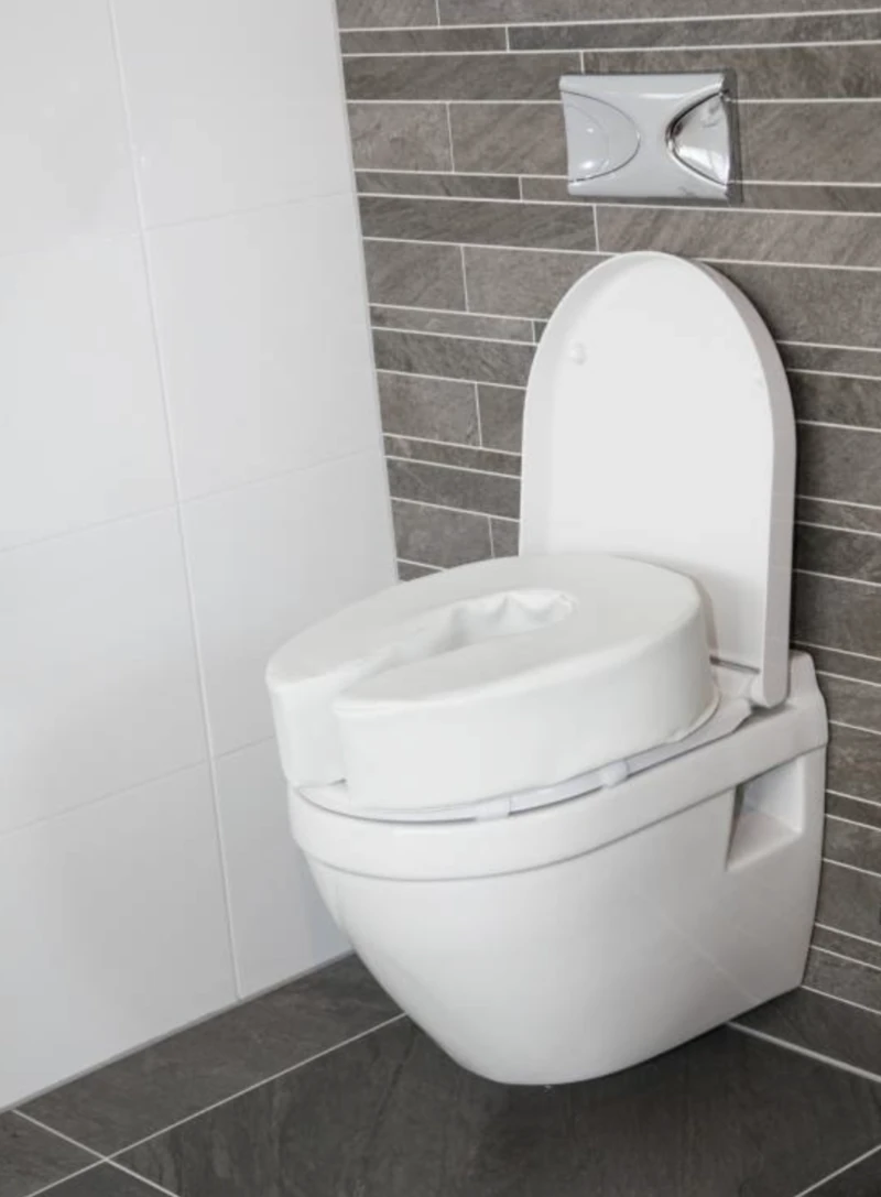 Padded raised toilet seat attached to a modern toilet in a bathroom.