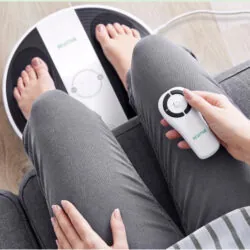 Person using Revitive foot massager with remote control.