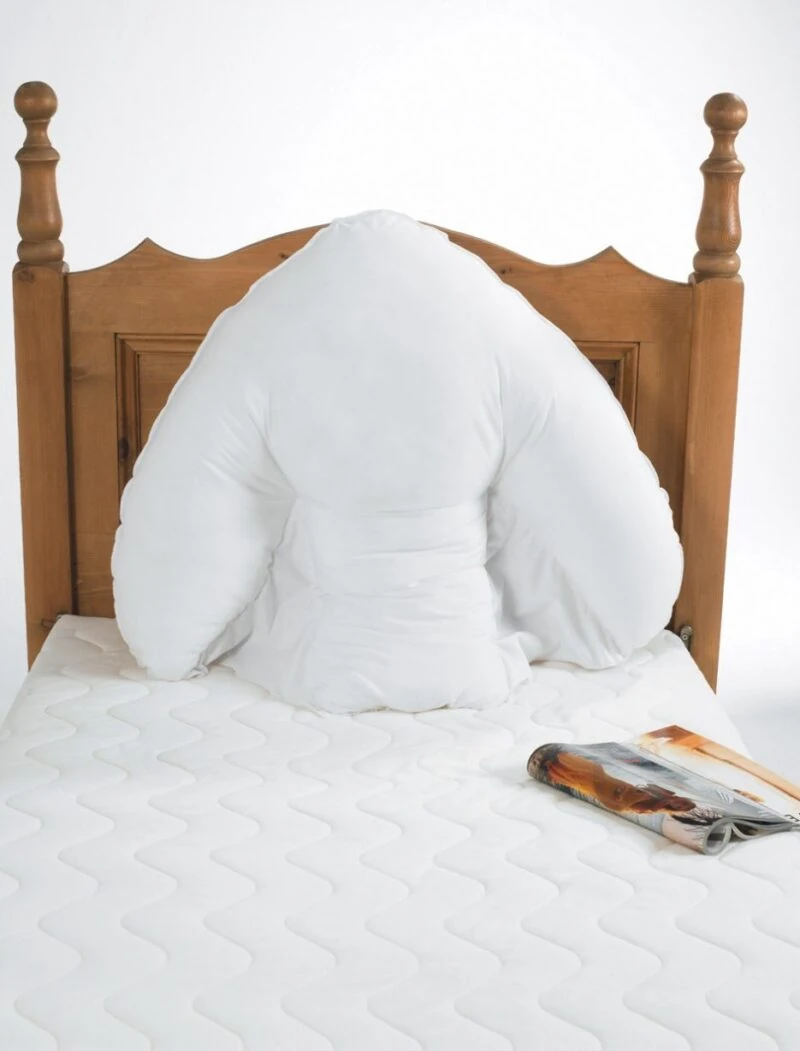 White batwing support pillow on a wooden bed with a magazine nearby.