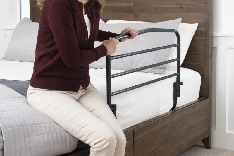 Person using a bed support rail attached to a wooden bed frame.