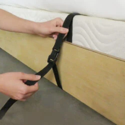 Hands securing a black strap to a bed frame.