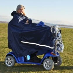 Person using a mobility scooter with a protective cape in an open field.