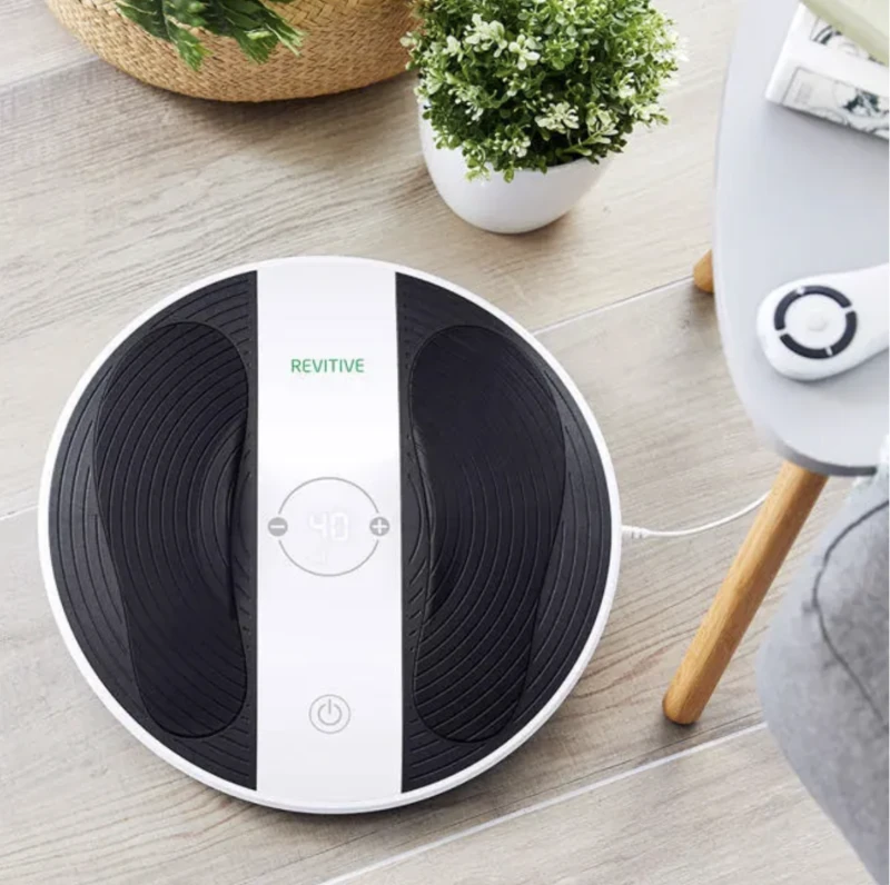 Revitive foot massager machine on a wooden floor next to a plant.