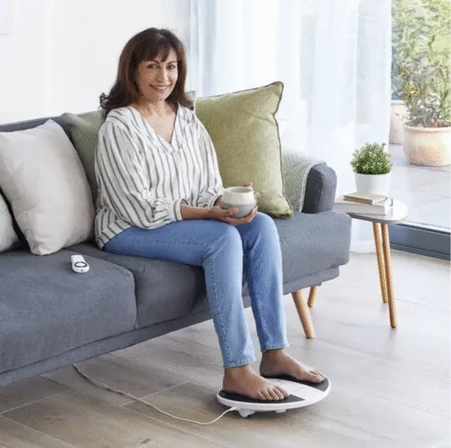 Woman sitting on a couch using a foot massager machine.