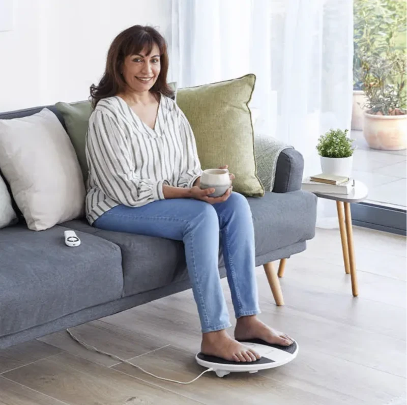 Woman sitting on a couch using a foot massager machine.