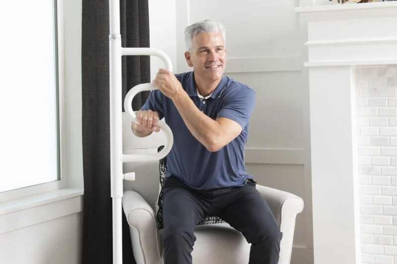 Man sitting and holding a white curved grab bar attached to a pole.
