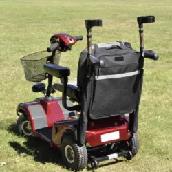 Red mobility scooter with a black bag and crutch holder on grass.