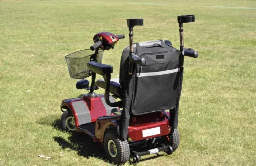 Red mobility scooter with a black bag and crutch holder on grass.