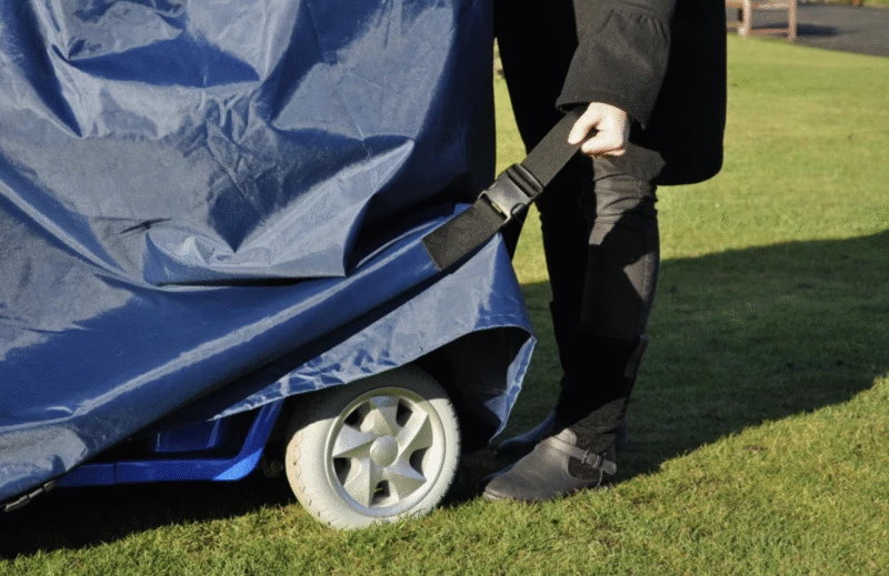 Person securing a navy waterproof cover over a mobility scooter wheel.