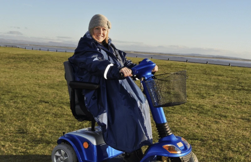 Person wearing a blue poncho on a mobility scooter outdoors.