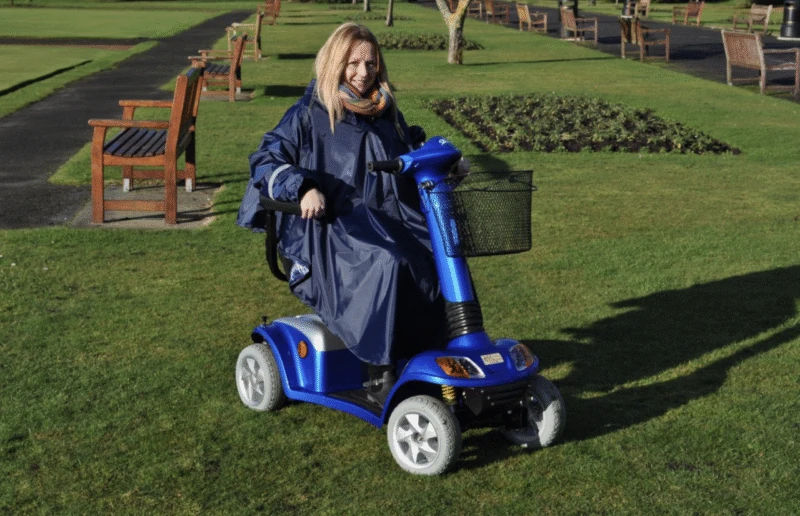Person wearing a blue poncho on a mobility scooter in a park.
