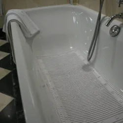 White anti-slip bath mat inside a bathtub with a towel on the edge.