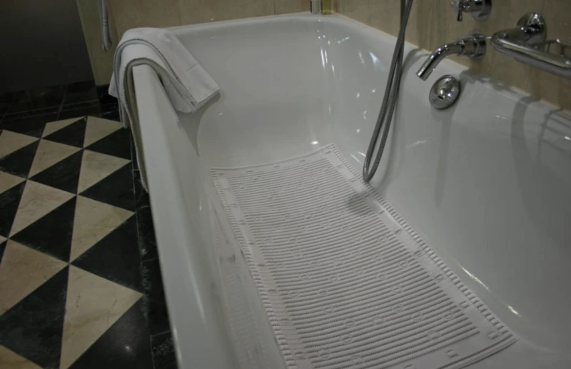 White anti-slip bath mat inside a bathtub with a towel on the edge.