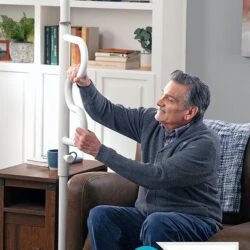 Man using a white security pole with a curved grab bar in a living room.