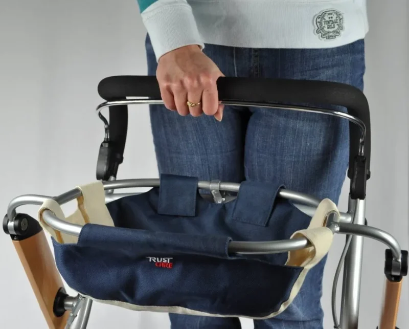 Person holding the handle of a Trust Care indoor rollator with a blue bag attached.