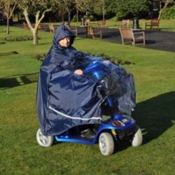 Person using a mobility scooter with a protective cape in a park.
