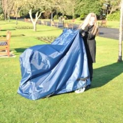 Person covering a mobility scooter with a navy waterproof cover in a park.