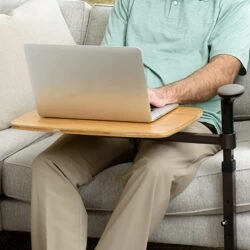 Person using a laptop on a swivel table attached to a sofa.