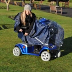 Person using a mobility scooter with a protective cape in a park.