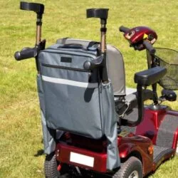 Mobility scooter with attached grey bag and crutch holder on grass.