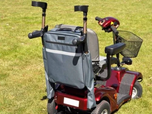 Mobility scooter with attached grey bag and crutch holder on grass.