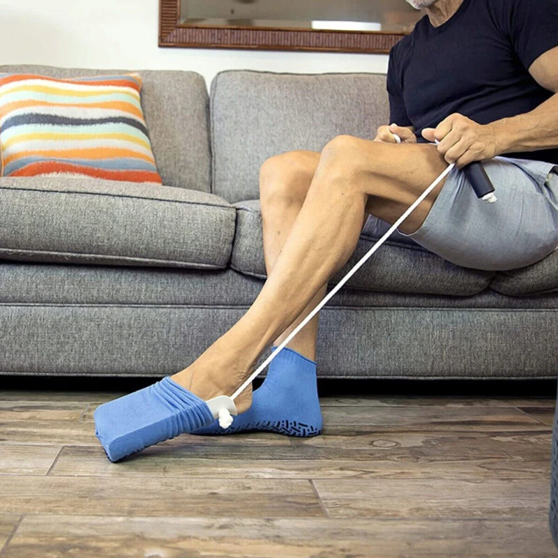 Person using a sock stocking aid to put on blue socks while seated on a couch.