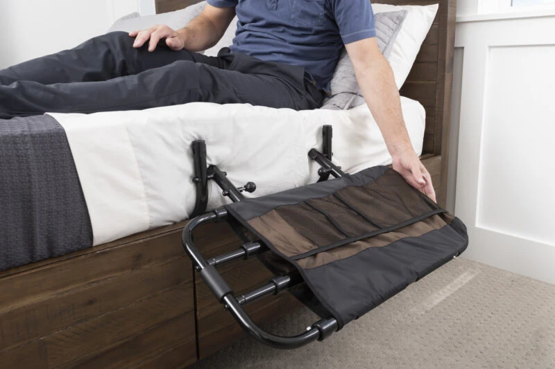 Person adjusting a bed rail with a pouch attached at the side of a bed.