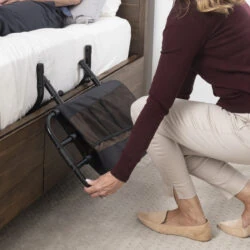 Person adjusting a bed rail with a pouch on a wooden bed frame.