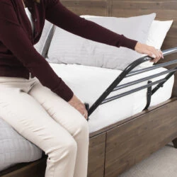 Person using a bed support rail attached to a wooden bed frame.