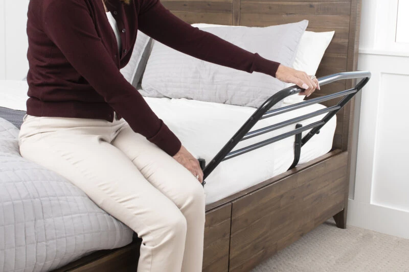 Person using a bed support rail attached to a wooden bed frame.