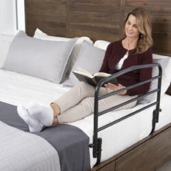 Person sitting on a bed with a safety rail, reading a book.