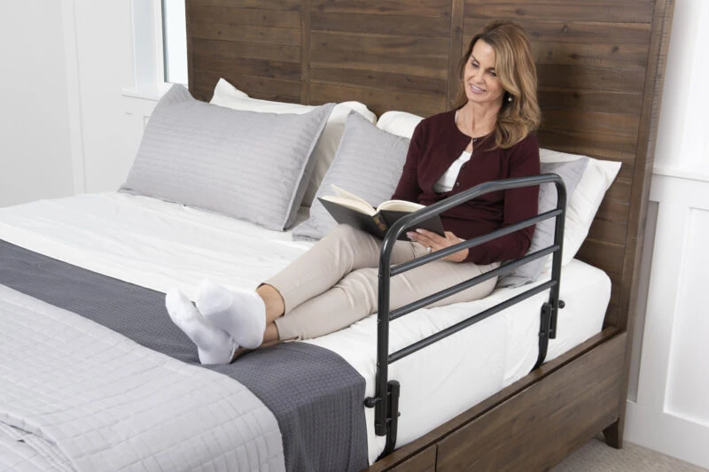 Person sitting on a bed with a safety rail, reading a book.