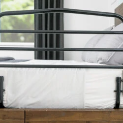 Black bed support rail attached to a bed with white sheets and gray pillows.