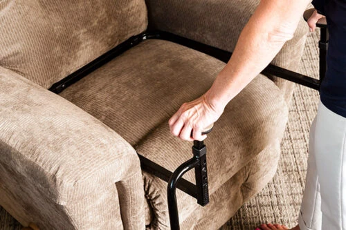 Person using a stand assist aid on a beige sofa.