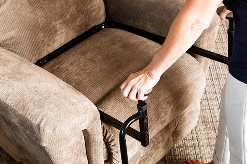 Person using a stand assist aid on a beige sofa.