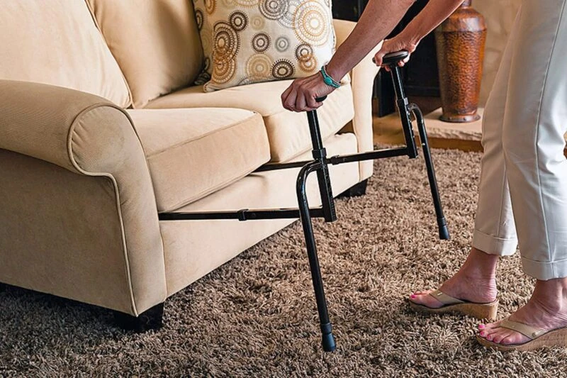 Person using a stand assist aid to rise from a sofa.