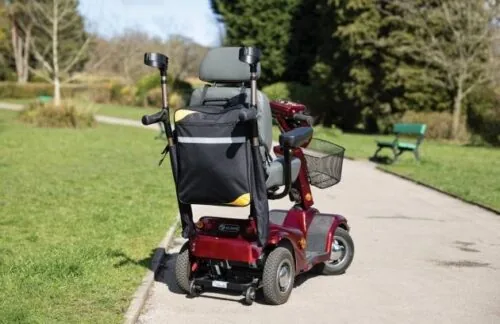Mobility scooter with attached bag and crutch holder on a park path.