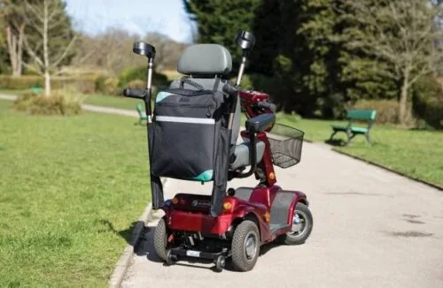Mobility scooter with a black bag and crutch holder on a park path.