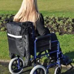 Person in wheelchair with a black mobility scooter bag attached.