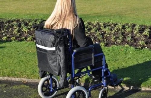 Person in wheelchair with a black mobility scooter bag attached.