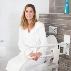 Woman sitting on toilet with folding bath rail installed.