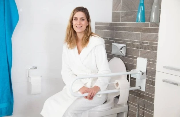 Woman sitting on toilet with folding bath rail installed.